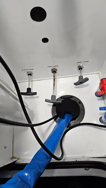 Black and grey tank valves with sewer hose connected during an RV waste system service call
