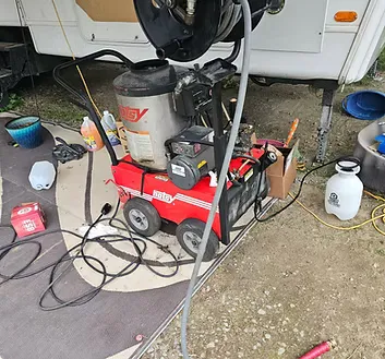 Pressure washer and cleaning supplies set up beside an RV before roof cleaning and reseal work